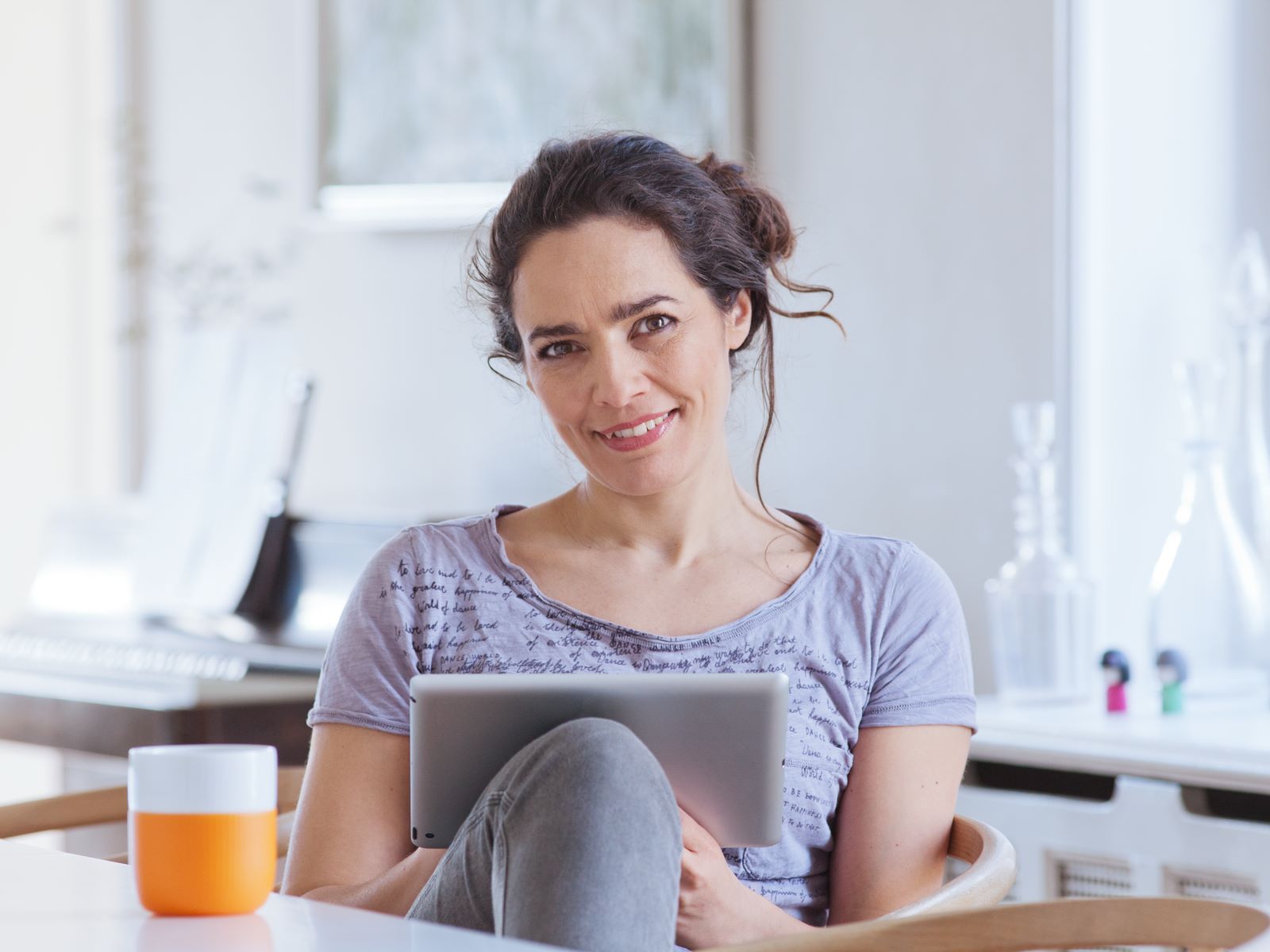 Kvinde i sidder i køkkenet og kigger på en tablet. Baggrunden er lys med køkkenredskaber og glasbeholdere.