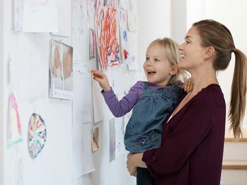 En mor og datter smiler, mens de ser på børnetegninger, der er hængt op på væggen.