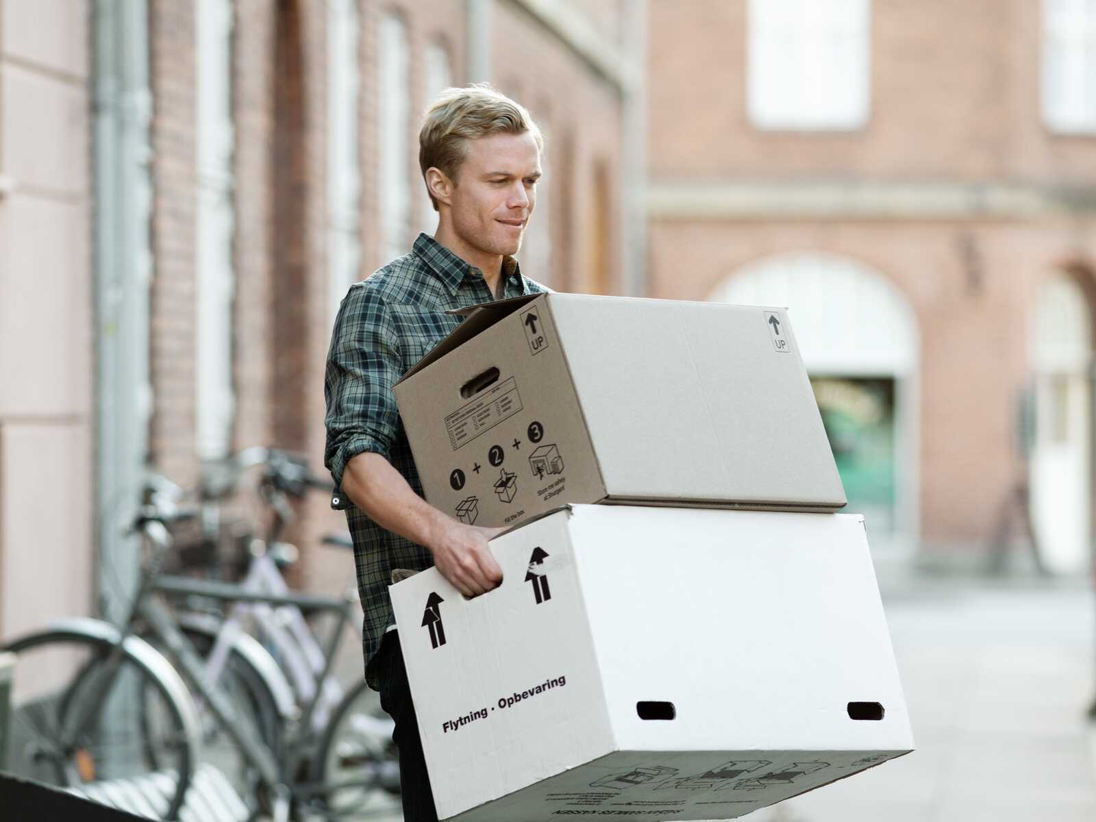 En ung mand bærer flyttekasser udenfor, mens han ser fokuseret ud.