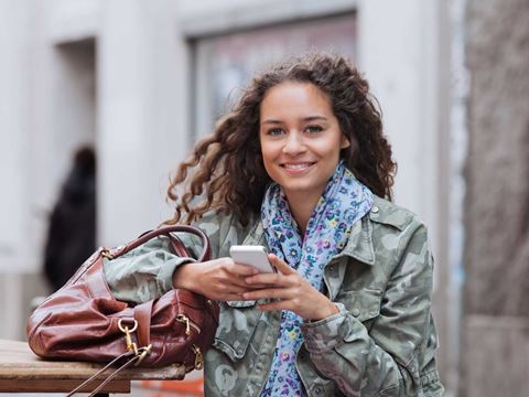 ung mørkhåret pige står udenfor og vind i håret og laver noget på hendes telefon, mens hun kigger op 