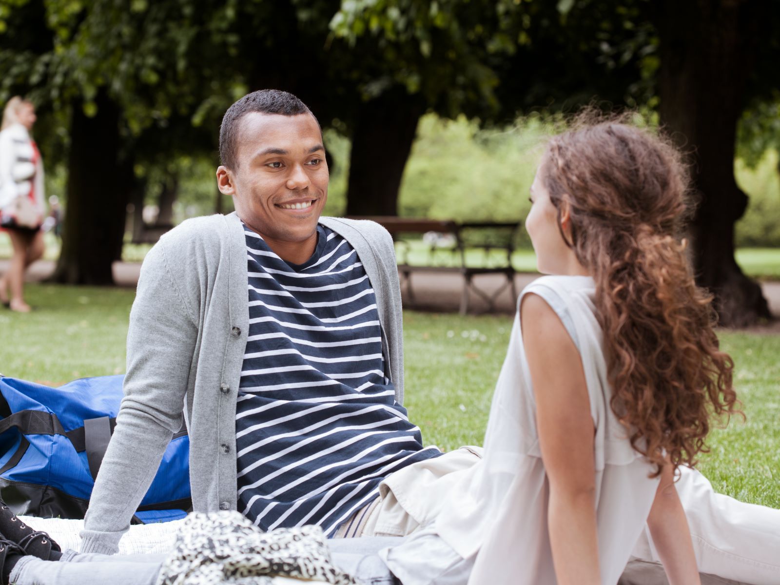 Ungt par sidder i en park og smiler til hinanden, mens de nyder hinandens selskab på en solrig dag.