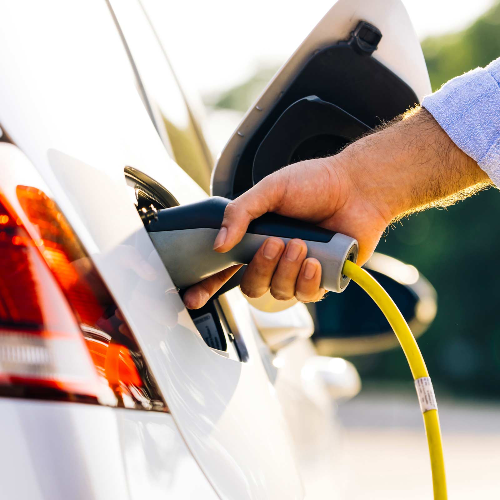 Person oplader elbil med et stik ved en ladestation.