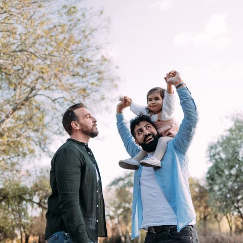 To mænd leger med barn på skulder i park.