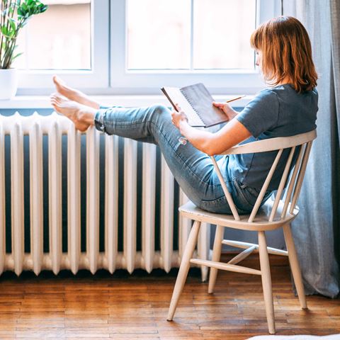 kvinde sidder på en stol med dine fødder i vindueskarm, og skriver i sin notesbog