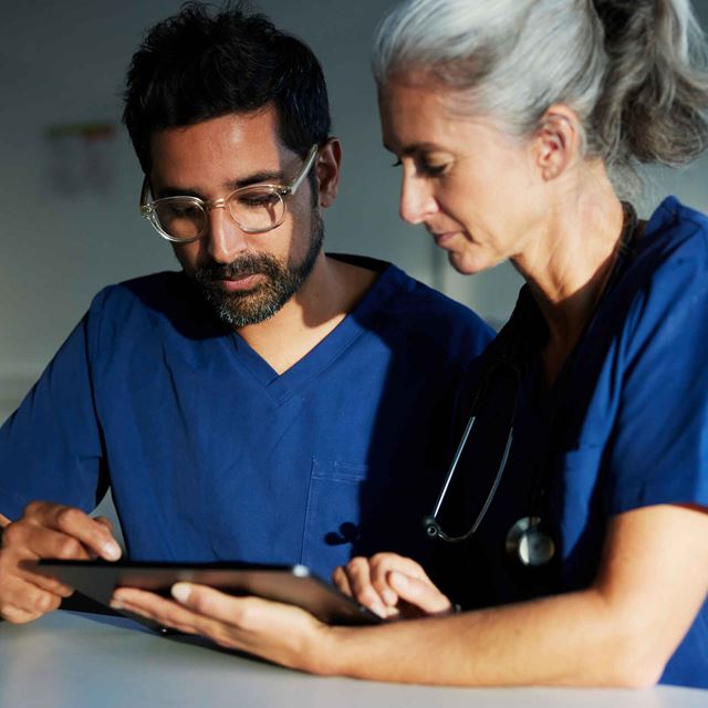 To læger i blå uniformer konsulterer sammen om patientdata på en tablet