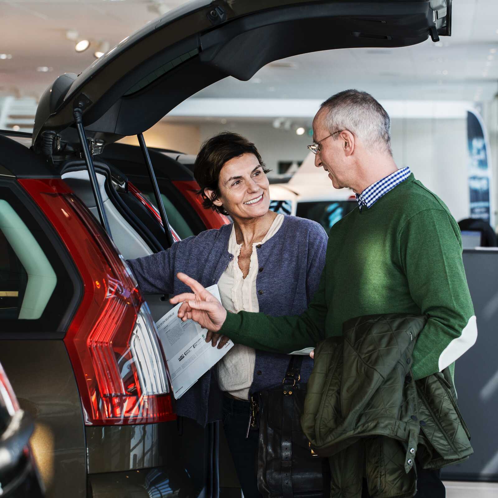 Et par undersøger bagagerummet på en bil i et showroom, mens de diskuterer detaljerne.