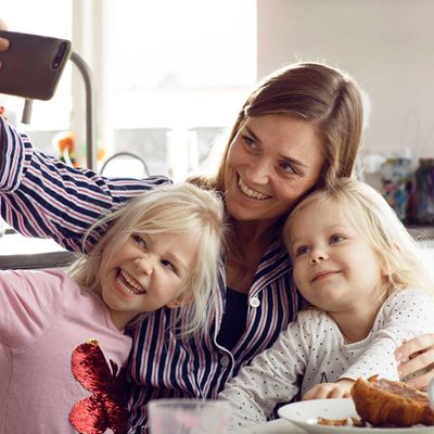 En mor tager en sjov selfie med sine to døtre i køkkenet, mens de alle smiler og laver ansigter.