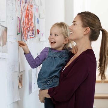 En mor og datter smiler, mens de ser på børnetegninger, der er hængt op på væggen.
