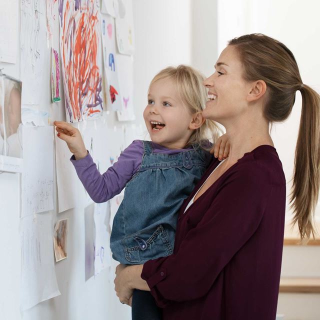 En mor og datter smiler, mens de ser på børnetegninger, der er hængt op på væggen.