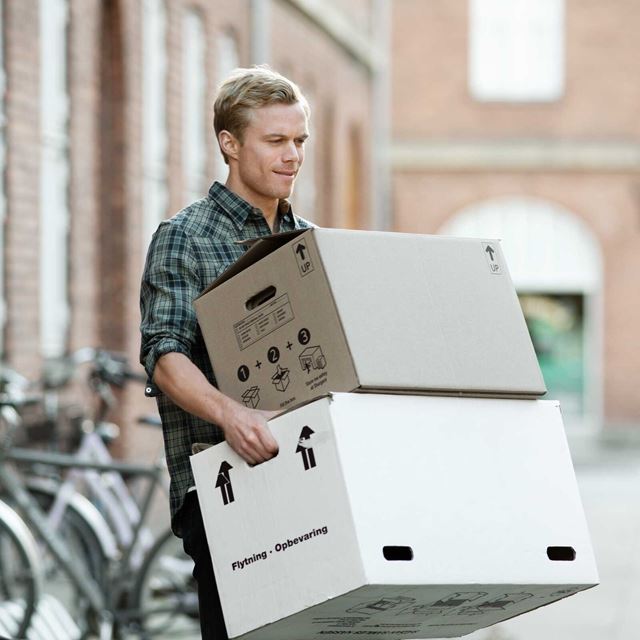 En ung mand bærer flyttekasser udenfor, mens han ser fokuseret ud.