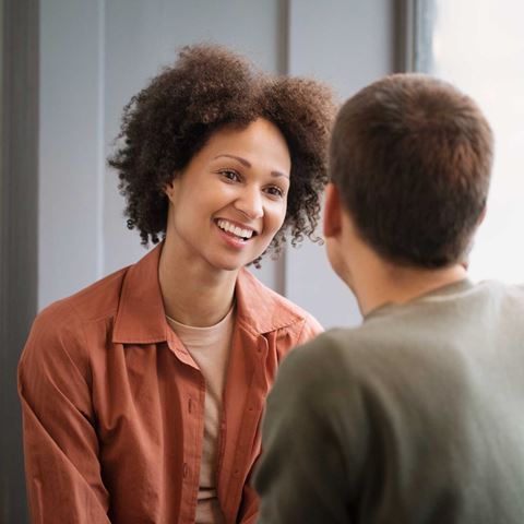 En kvinde i en rødbrun skjorte smiler til sin samtalepartner under en samtale.