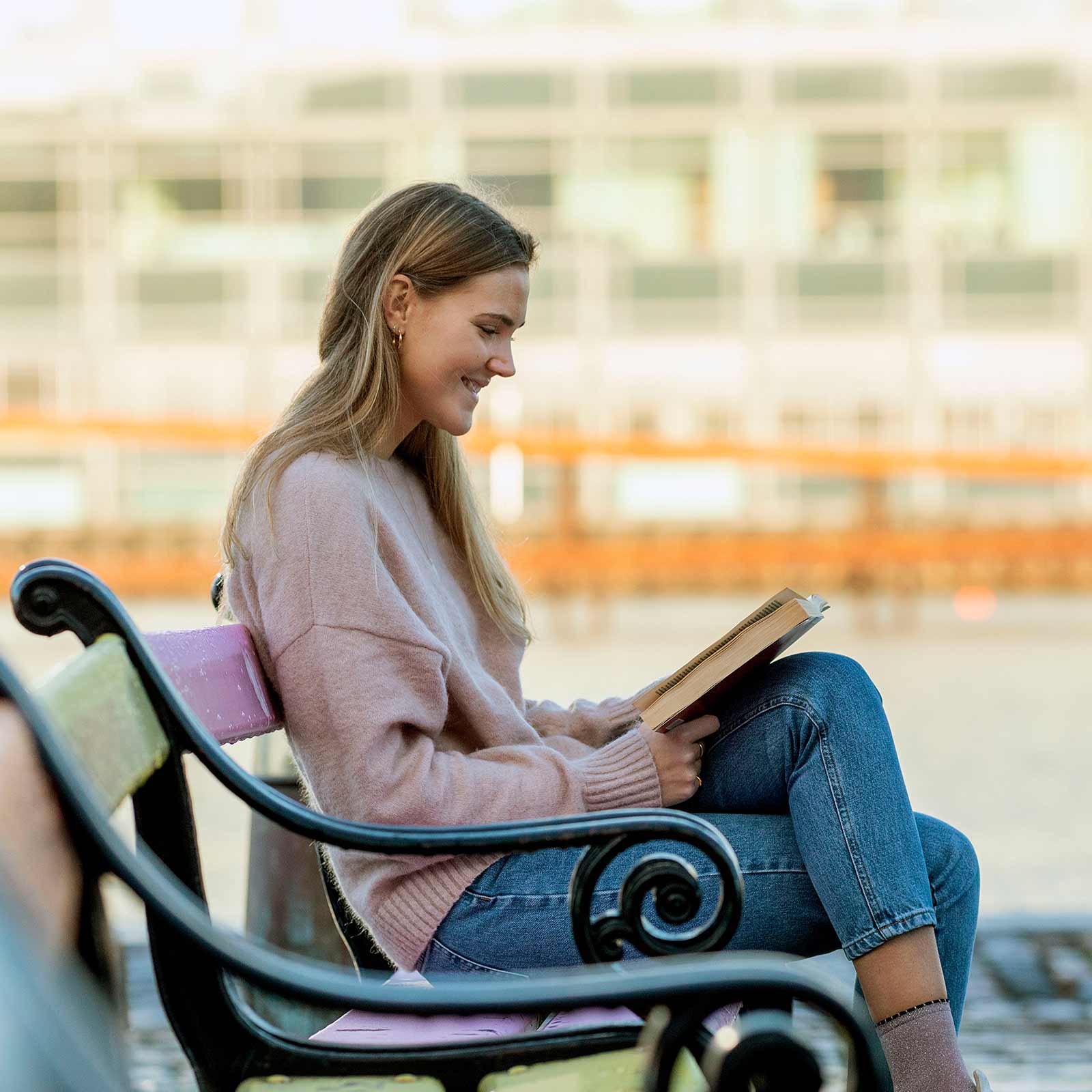 Ung kvinder læser bog på bænk