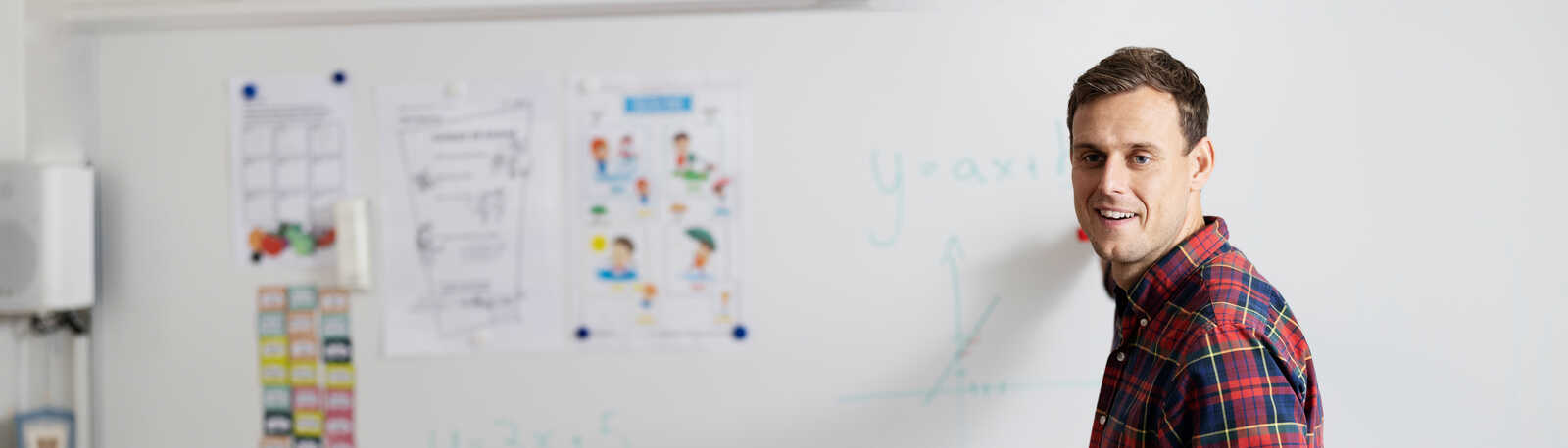 ung mand står ved en hvid tavle og underviser en klasse i en rød skjorte 