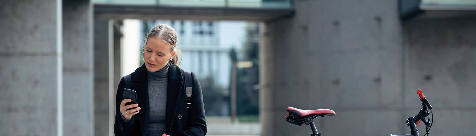 En kvinde sidder ved siden af sin cykel, spiser et æble og kigger på sin telefon med en kop kaffe ved siden af sig.