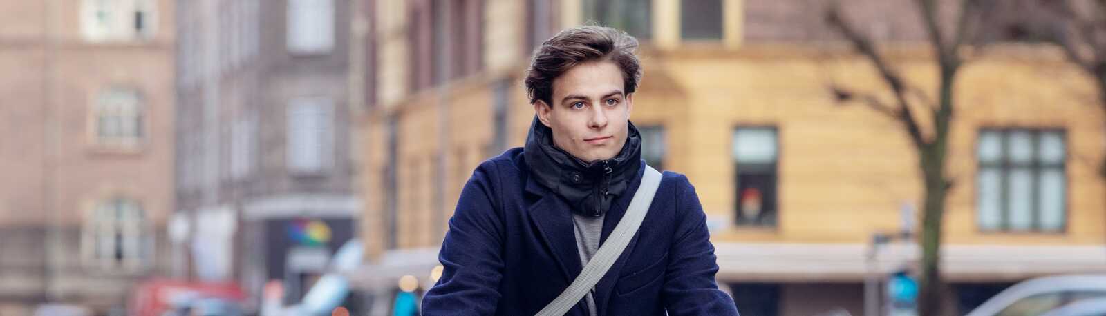 Ung mærket håret fyr cykler med sin blå jakke udenfor i efterårsvejret. 