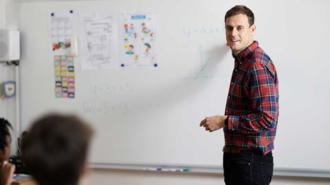 ung mand står ved en hvid tavle og underviser en klasse i en rød skjorte 