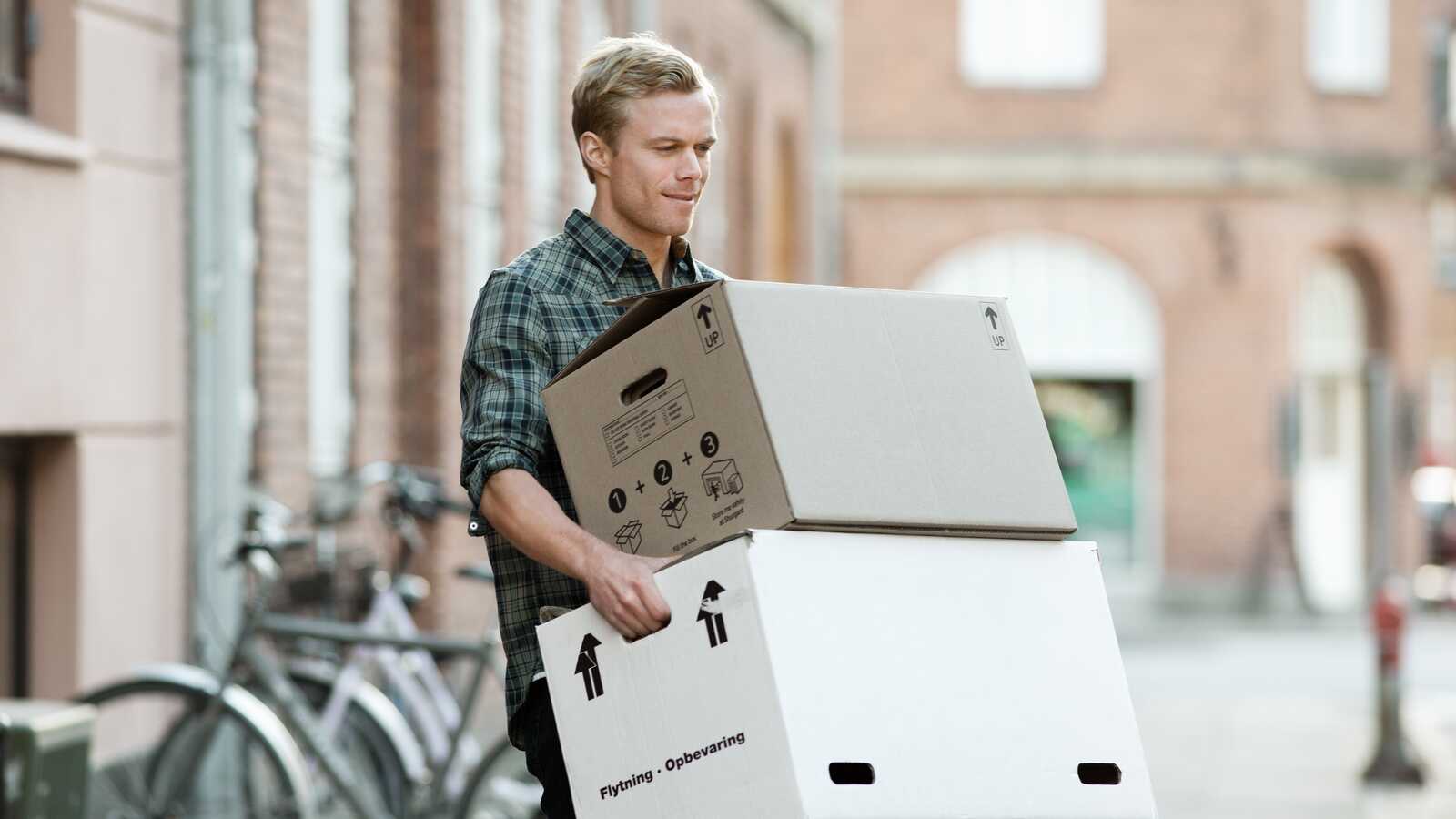 En ung mand bærer flyttekasser udenfor, mens han ser fokuseret ud.