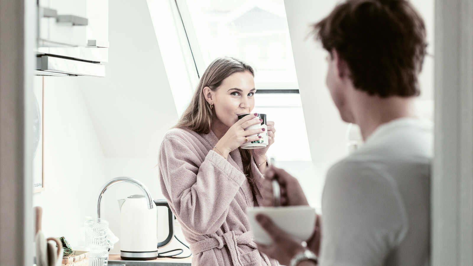 Unge kvinde drikker kaffe i køkkenet med sin kæreste