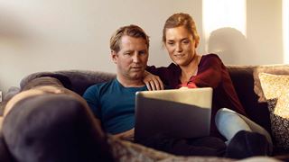 Par sidder i sofa og kigger på PC